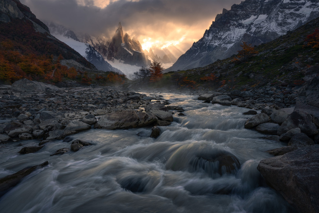 Light rays pour into view from a narrow opening in the clouds as rushing water and reflected light lead the way to Cerro Torre.