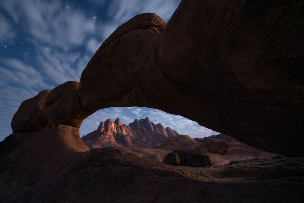 Spitzkoppe mountains illuminated by a full moon through an arch in Namibia